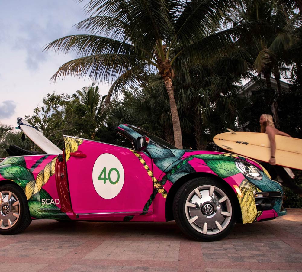 Guy with surfboard standing next to colorfully painted car 